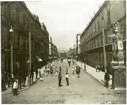 Vista de la Calle 5 de Mayo antes de su ampliación. Al fondo se observa el Teatro Nacional. Álbum <em>La Capital de México,</em> Colección Biblioteca Manuel Arango, Biblioteca Francisco Xavier Clavigero, Universidad Iberoamericana, Ciudad de México.